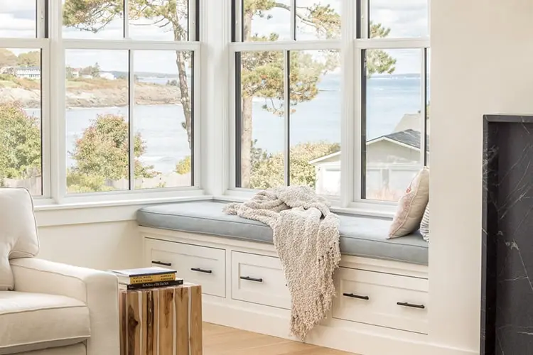 Vaulted living room with fireplace and wall of windows in a Cape Elizabeth, Maine home by Codere Construction