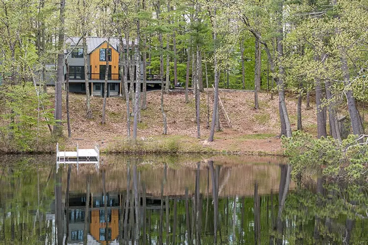 Lake house exterior seen across the water among tall pines – Lake House project, Windham, Maine, near Raymond