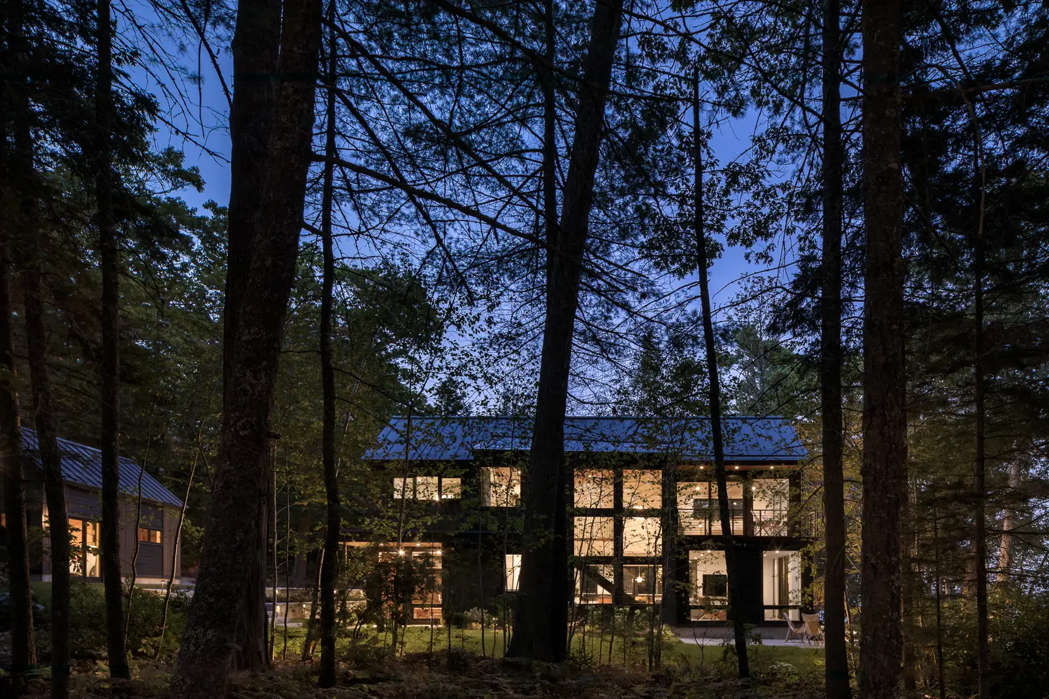 Modern home seen through the trees at night – Whites Cove project, Yarmouth, Maine, near Freeport