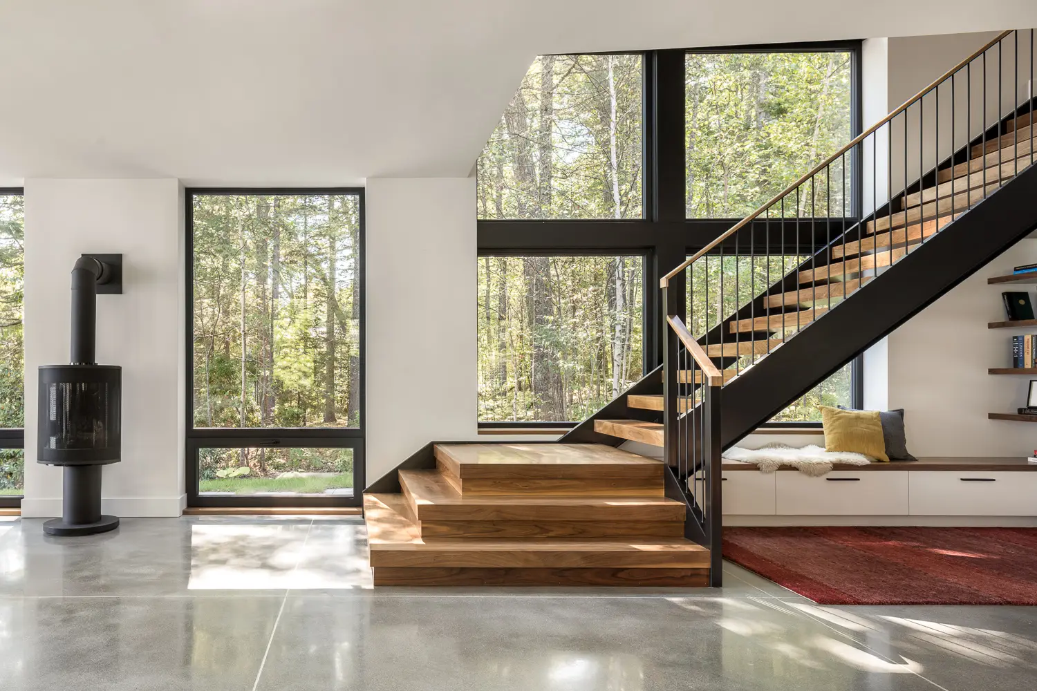 Living area with wood stove and floating staircase – Whites Cove net-zero home, Yarmouth, Maine